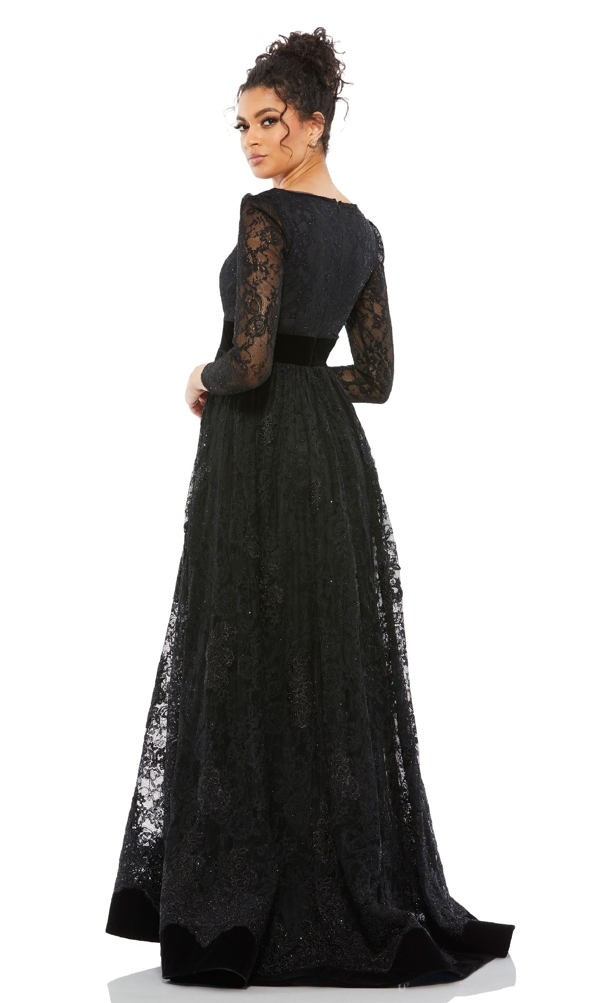 A woman stands looking over her shoulder, wearing the Mac Duggal 67861 long black lace formal dress with long sleeves and a black belt.